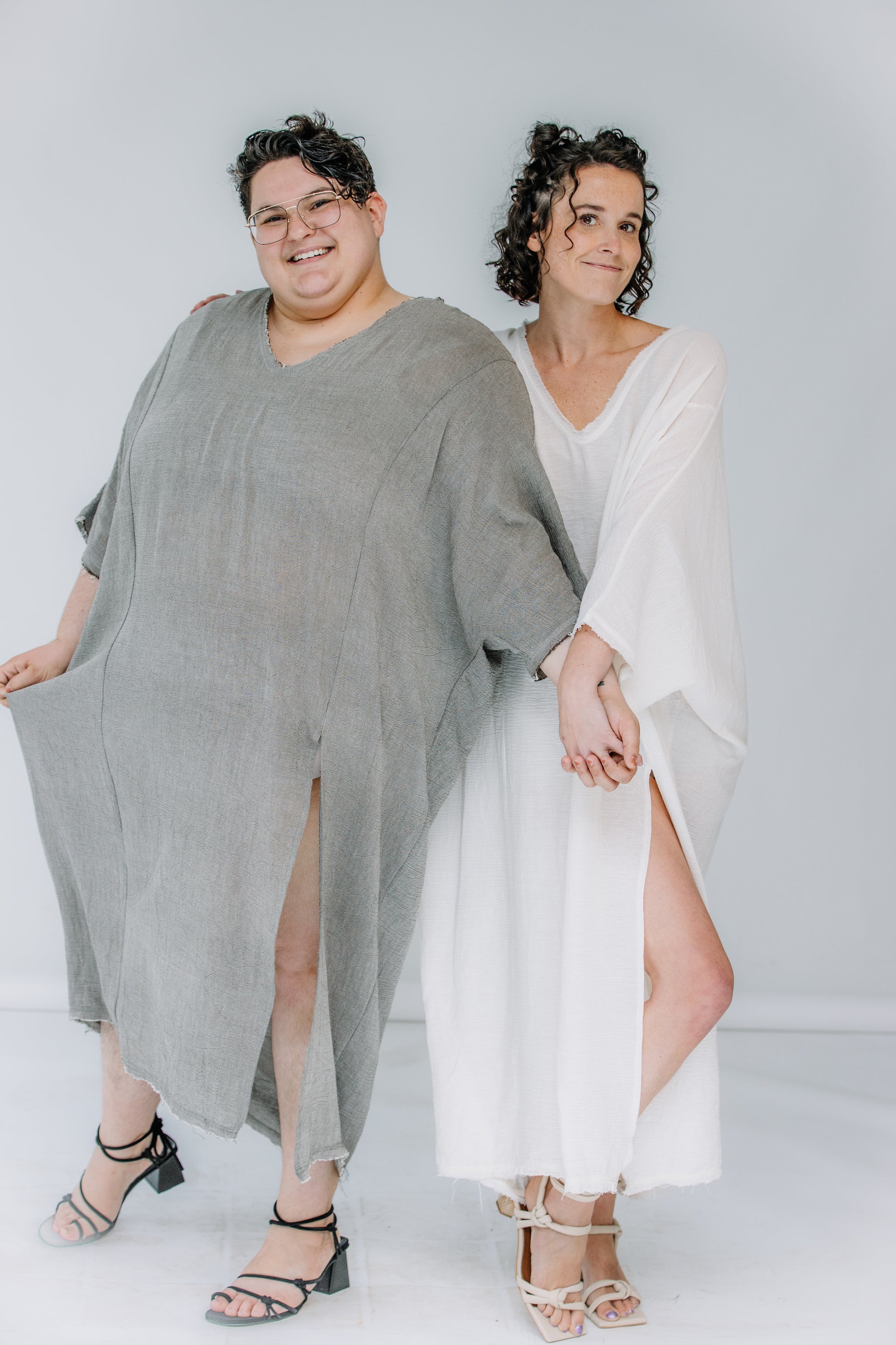 jules and lacey both wear the sile maxi caftan. jules has short dark hair, and they are wearing khaki with black sandals. lacey has dark curly spacebuns and wears the caftan in white with the creative ivory heels.