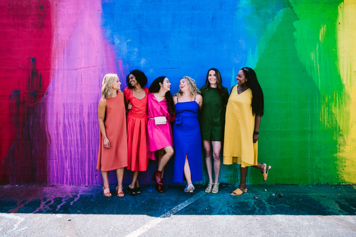 six young women in front of rainbow wall dressed in corresponding colors for basic.