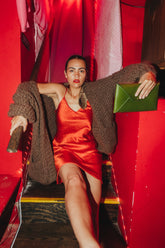 phoebe is wearing the danielle dean little red dress with the nia thomas lulua cardigan. she is staring directly into the camera and is holding an elidia the label green clutch pursee.