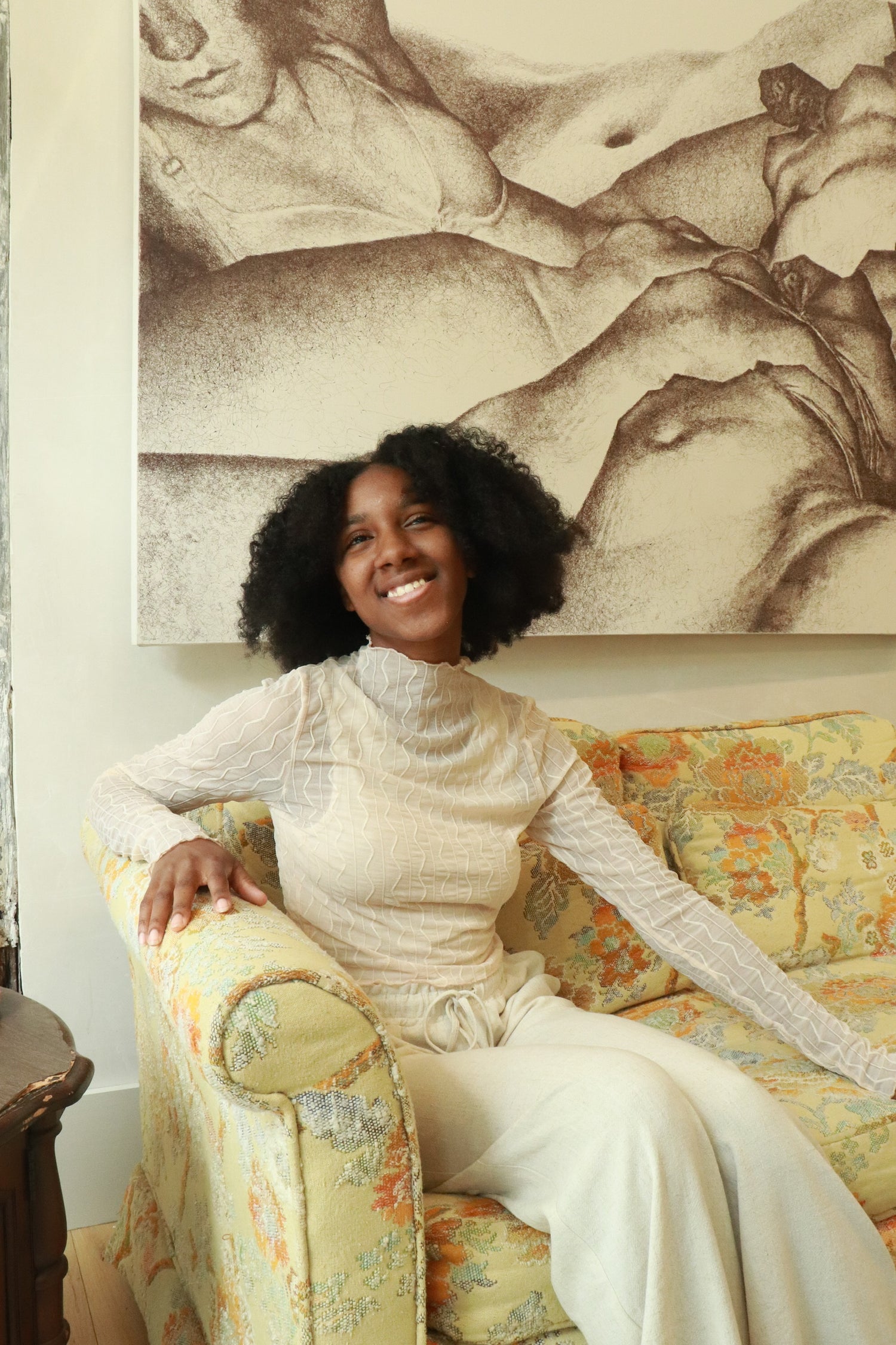 sonya smiles sitting on a vintage yellow couch wearing the abra jacquard top 