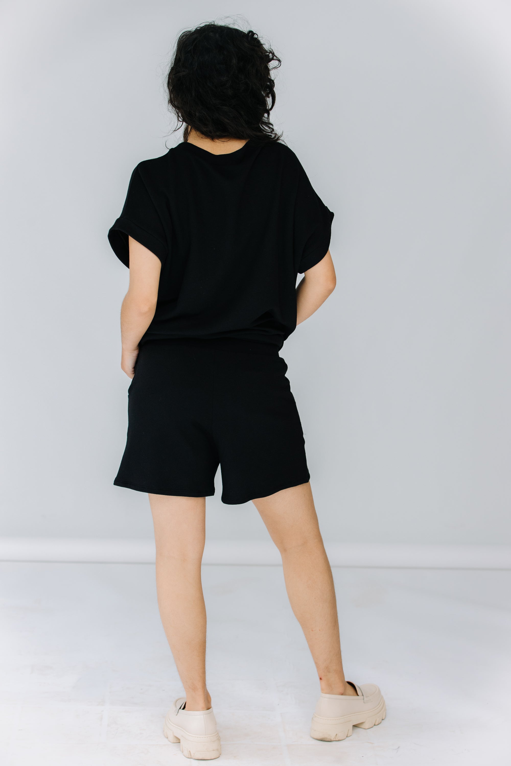 gabby wears the corinne collection siena shorts in black with the ava tunic in black and alohas trailblazer loafers.