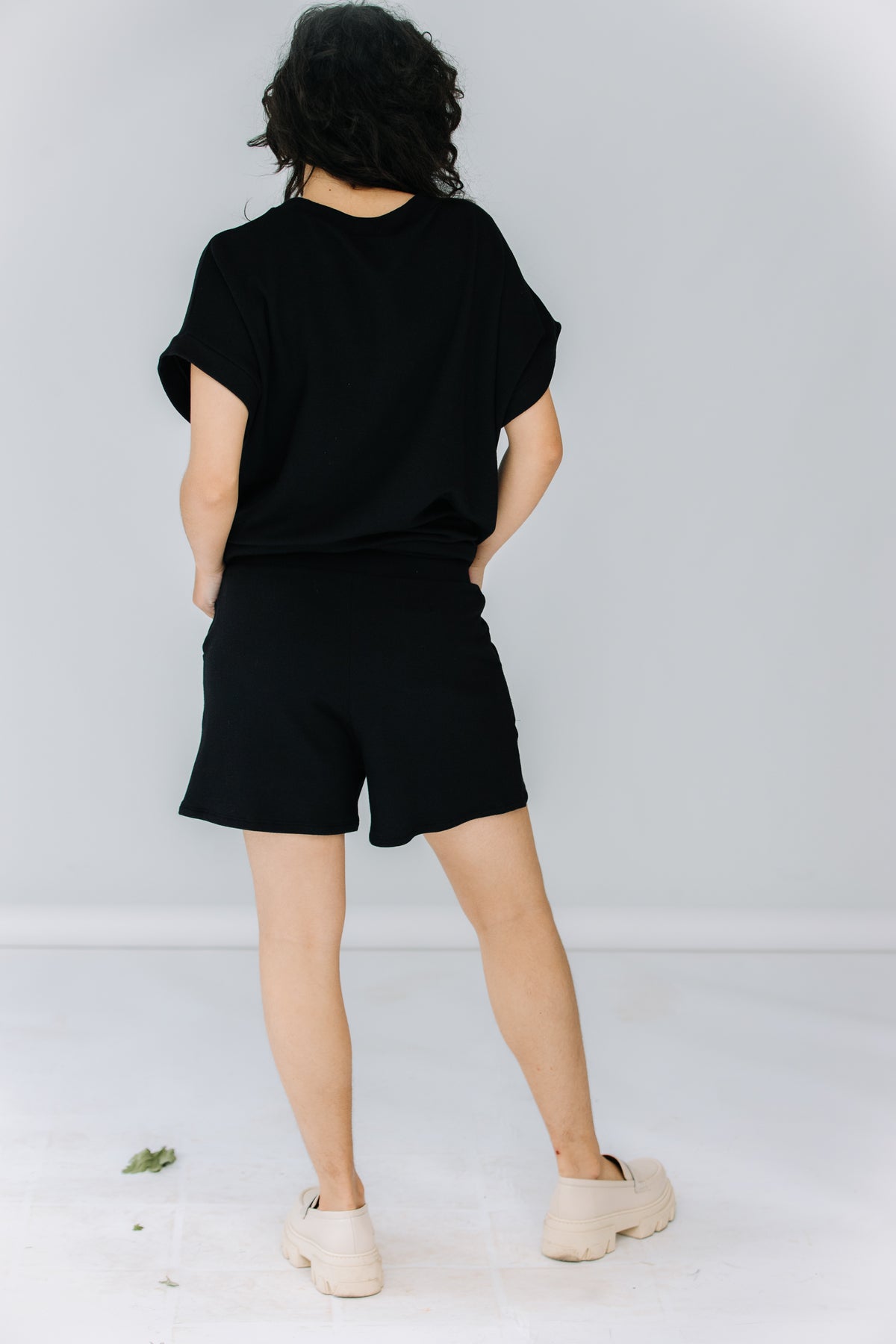 gabby wears the corinne collection siena shorts in black with the ava tunic in black and alohas trailblazer loafers.