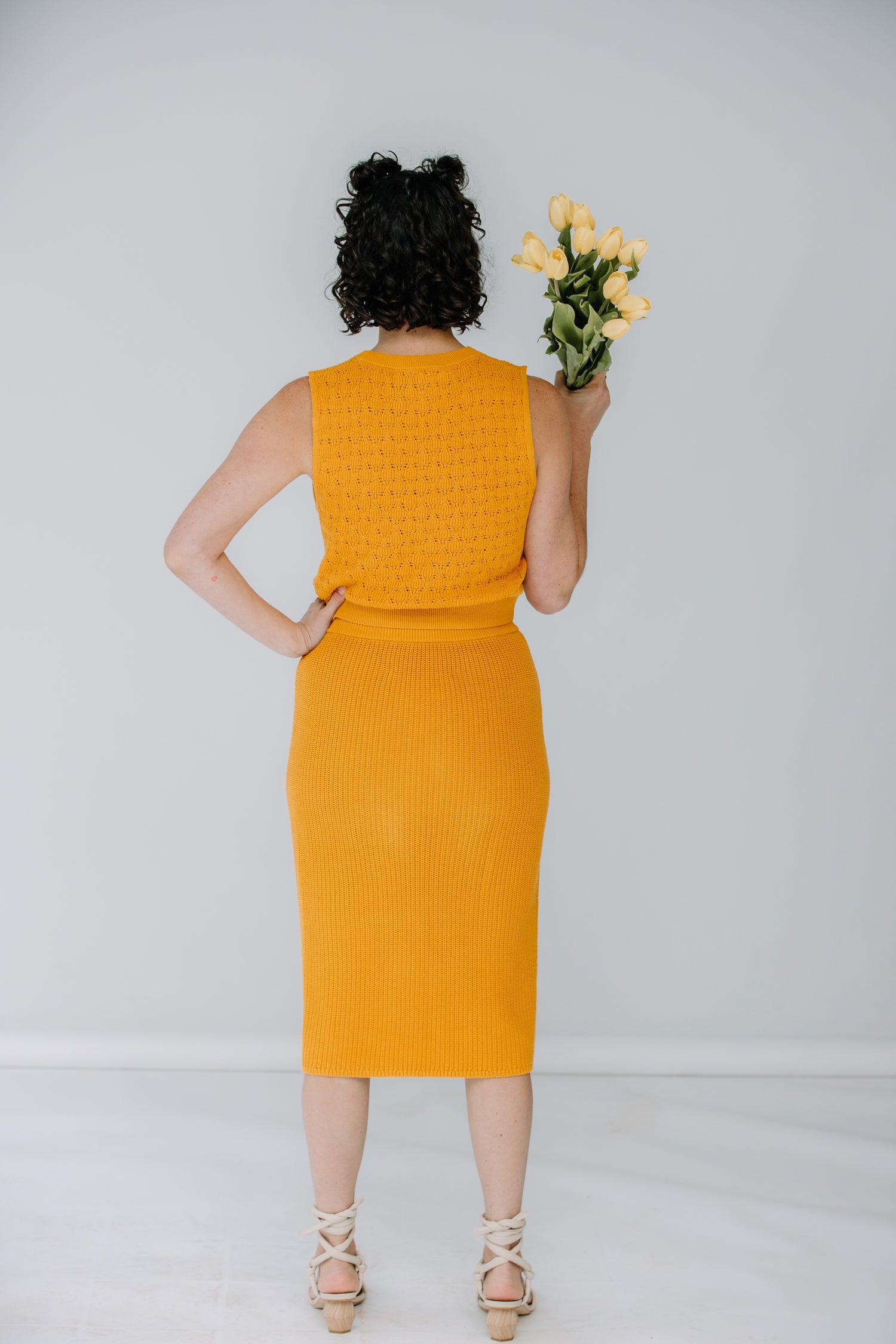 lacey wears the pointelle top and ribbed midi skirt in marigold by mr mittens. she is holding yellow tulips and has aloha creative ivory heels on.