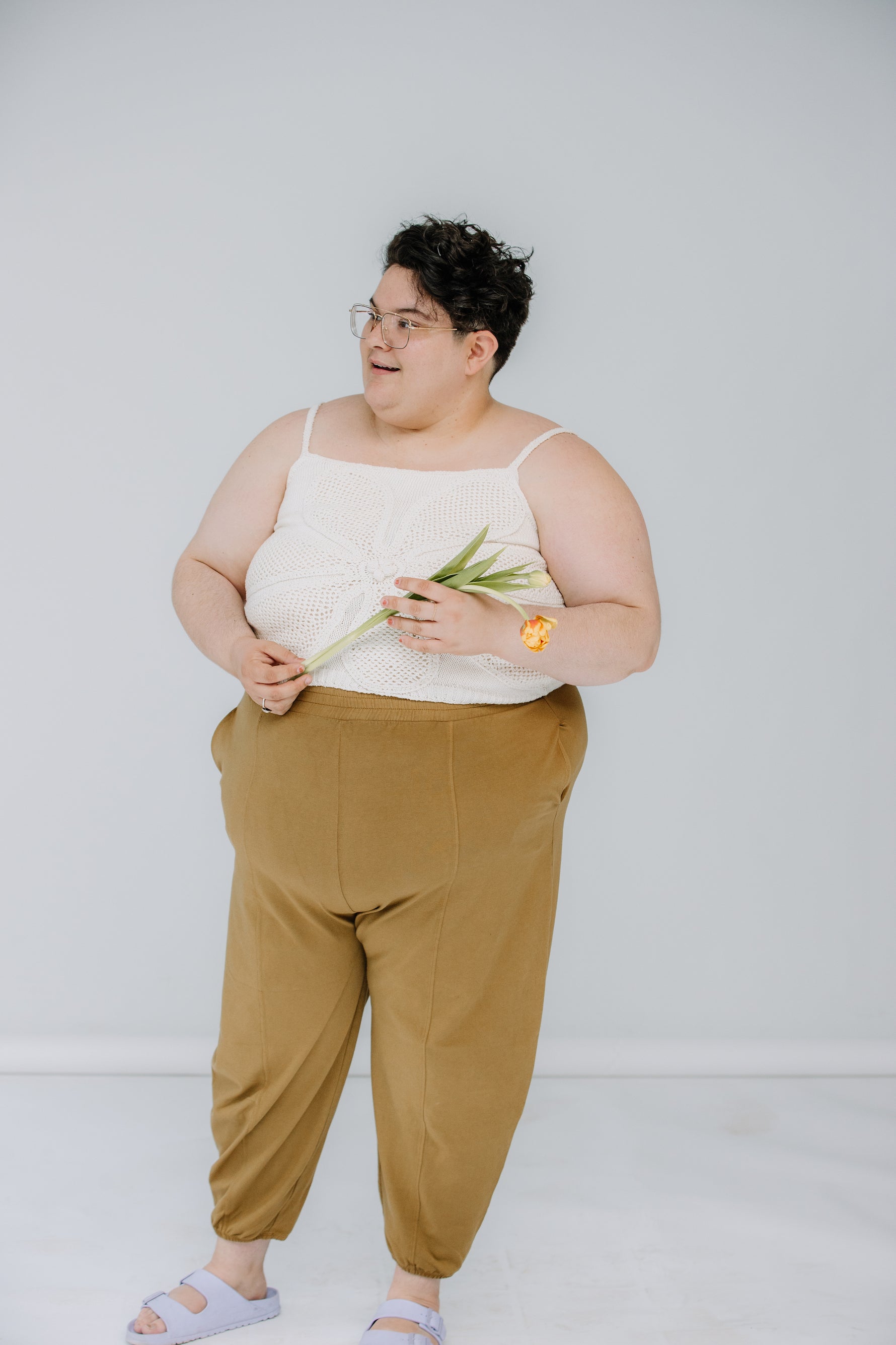 jules and lacey model the lingua franca crochet flower tank in ivory. jules is wearing theirs with mustard day lantern pants, and lacey has on kaarem sua trousers. they are both wearing sandals and soft smiling.