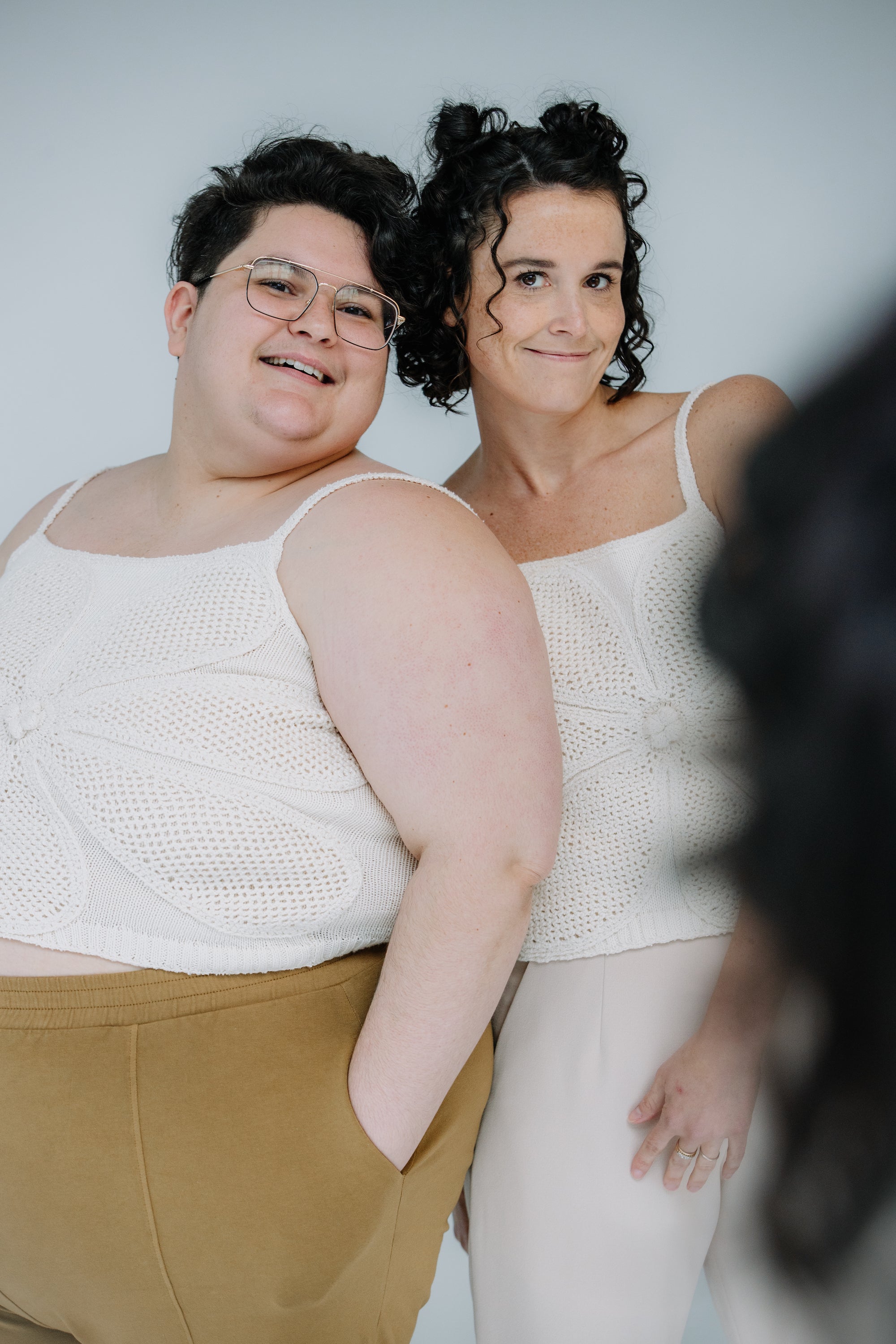 jules and lacey model the lingua franca crochet flower tank in ivory. jules is wearing theirs with mustard day lantern pants, and lacey has on kaarem sua trousers. they are both wearing sandals and soft smiling.