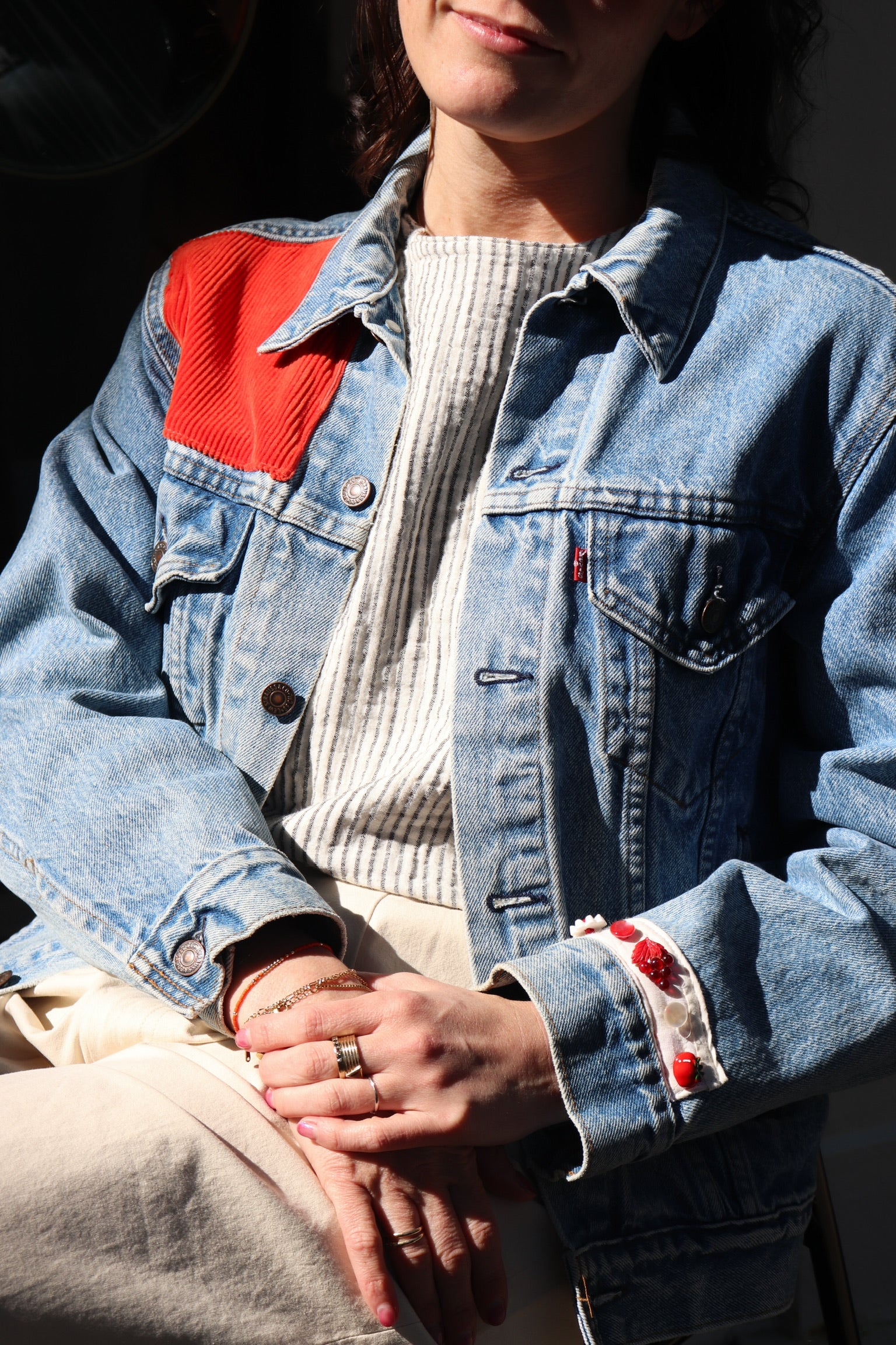 detail of a one of a kind freckled past denim jacket with a red corduroy upper left panel and vintage red flower bead detail at the wrist.