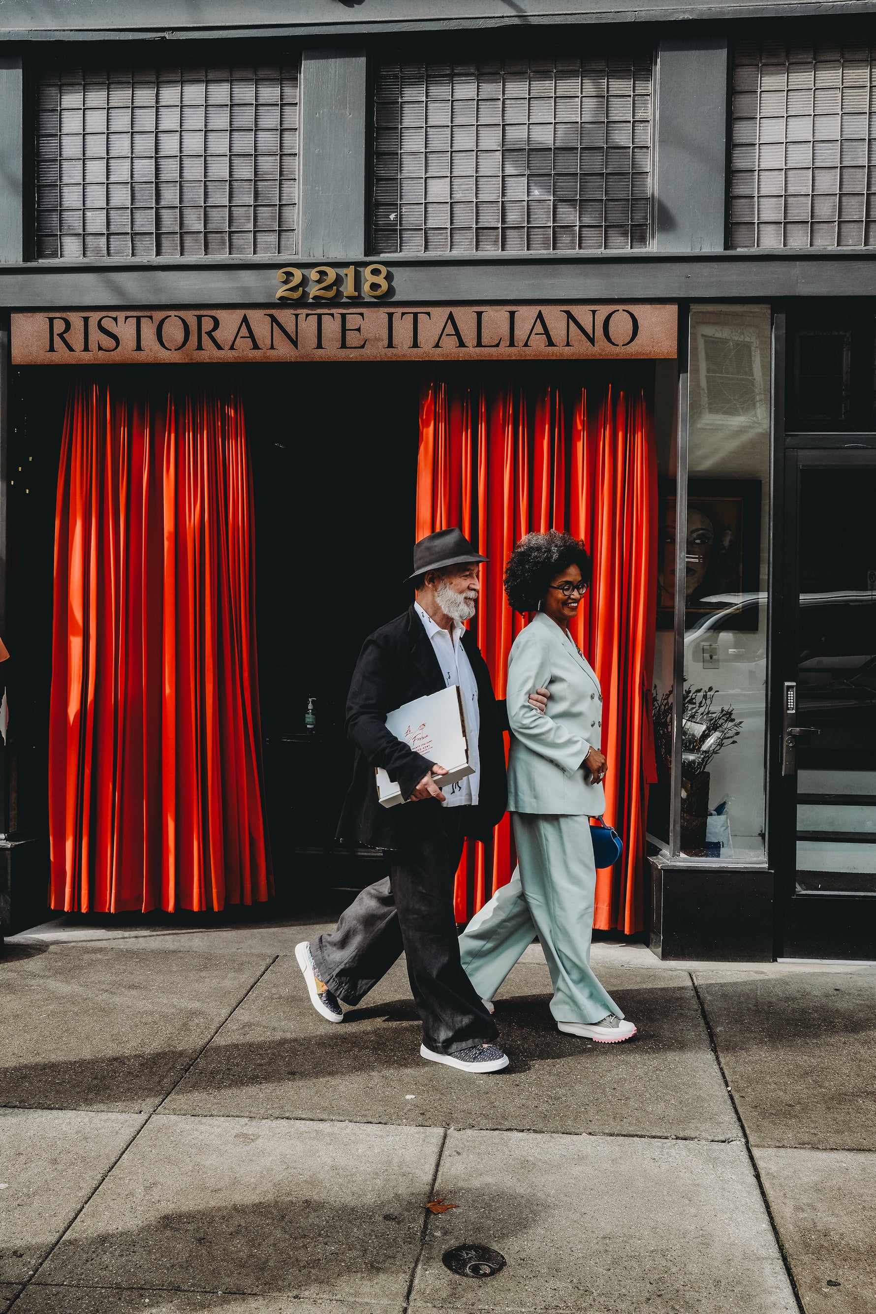 steve is wearing a black bowler cap and black suit while valerie wears the dylan pants + freya blazer from basic.