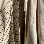 Beige jacket with black polka dot pattern on a hanger against a gray wall