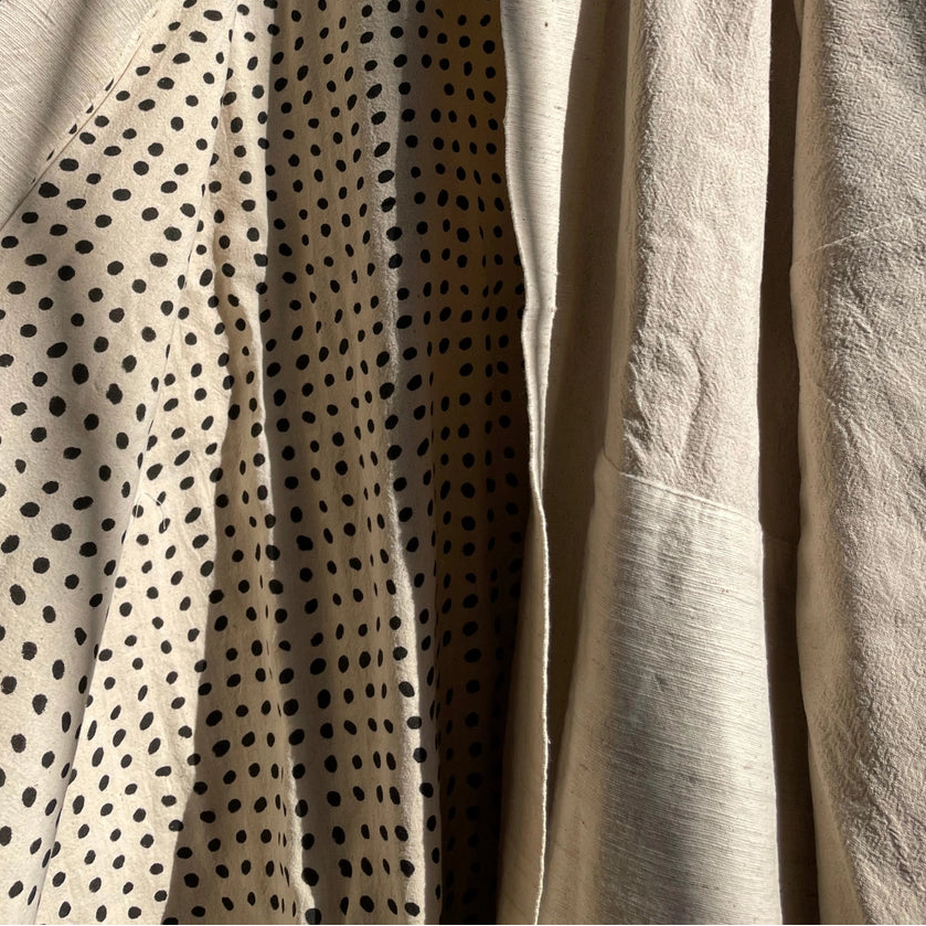 Beige jacket with black polka dot pattern on a hanger against a gray wall