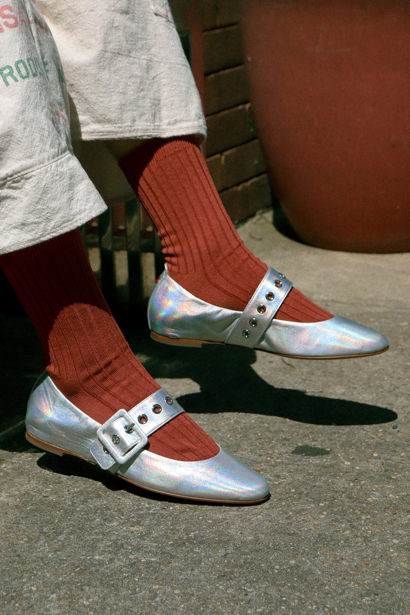 Person wearing silver shoes with red socks on a concrete surface.
