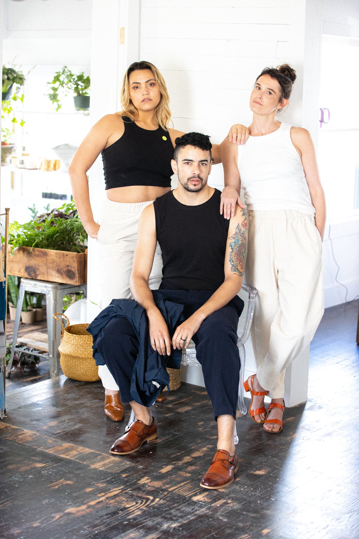 two women stand wearing corresponding jean jones amelia tanks behind reggie wearing the szeki textured linen tank. they're all wearing the unisex trouser.