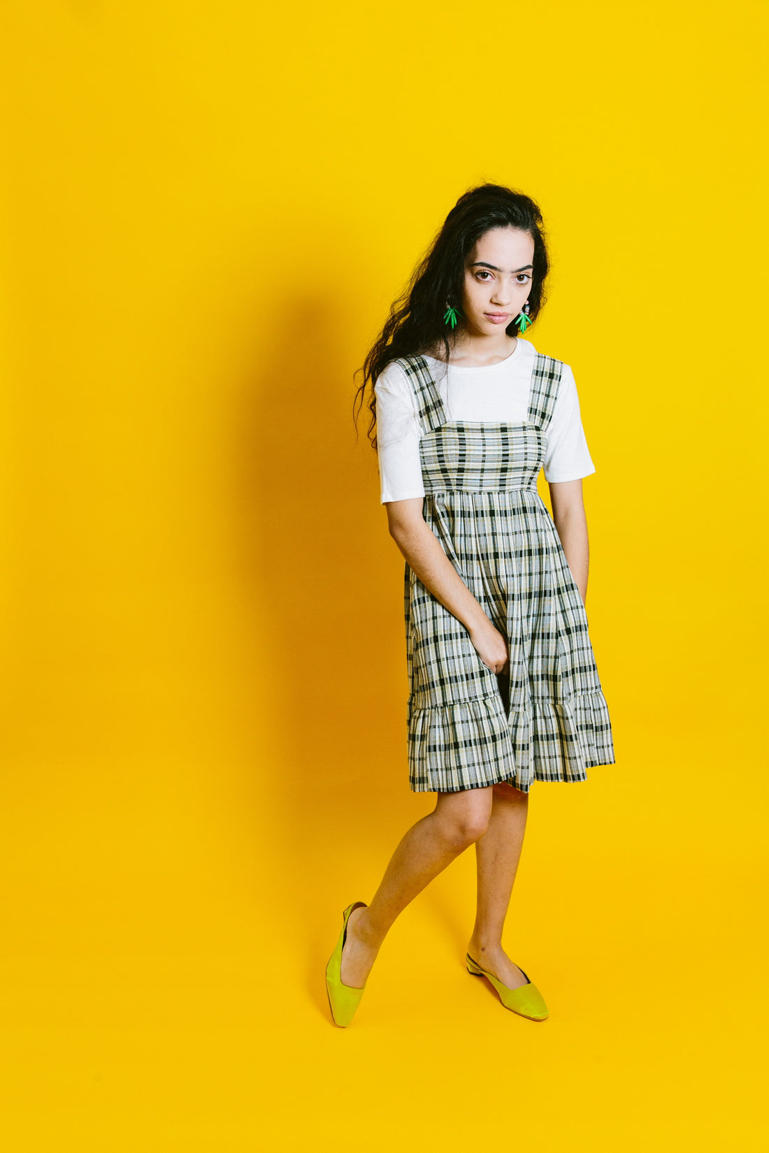 gabby wears the shaina mote classic tee under a plaid dress in front of a yellow background | a basic shop