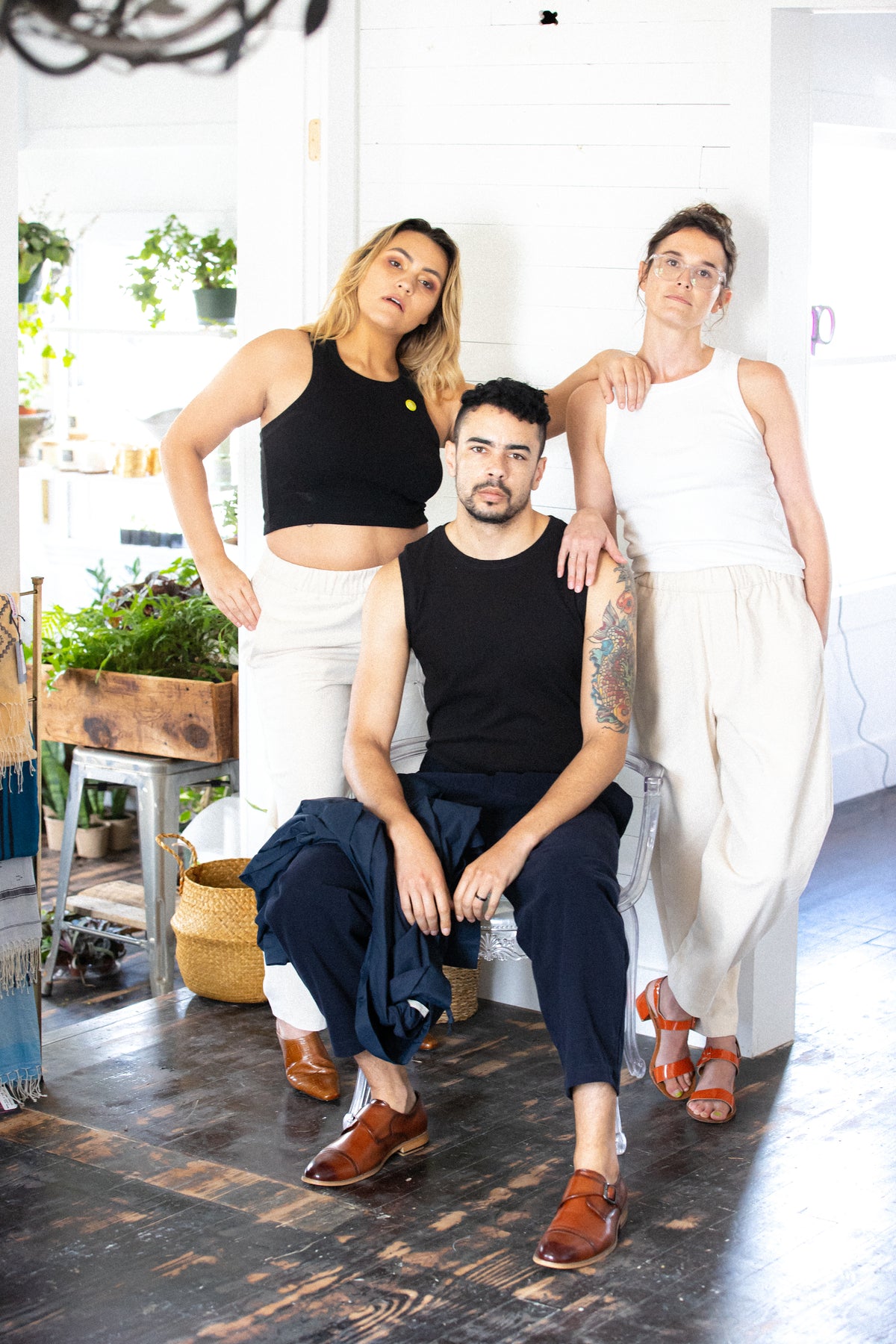 two women stand wearing corresponding jean jones amelia tanks behind reggie wearing the szeki textured linen tank. they're all wearing the unisex trouser.