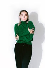 lemon stands with her hands in her pockets wearing a paloma wool sweater and été noir high-waisted alpaca trousers in front of a white background - basic. 