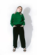 lemon stands with her hands in her pockets wearing a paloma wool sweater and été noir high-waisted alpaca trousers in front of a white background - basic. 